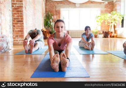 fitness, sport and healthy lifestyle concept - group of people doing yoga seated forward bend pose on mats at studio. group of people doing yoga forward bend at studio