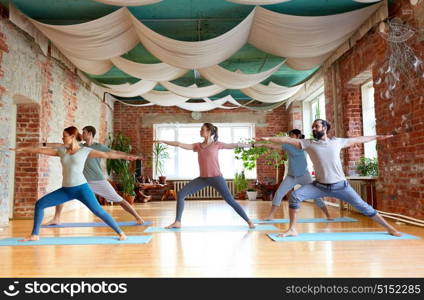 fitness, sport and healthy lifestyle concept - group of people doing yoga in warrior pose at studio. group of people doing yoga warrior pose at studio