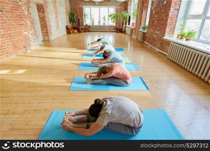 fitness, sport and healthy lifestyle concept - group of people doing yoga seated forward bend pose on mats at studio. group of people doing yoga forward bend at studio