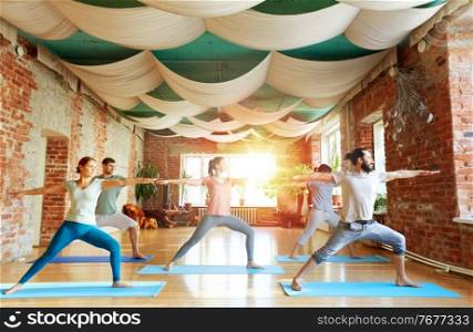 fitness, sport and healthy lifestyle concept - group of people doing yoga in warrior pose at studio. group of people doing yoga warrior pose at studio