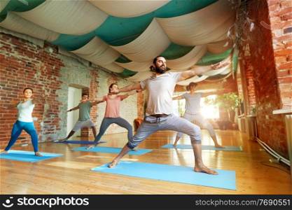 fitness, sport and healthy lifestyle concept - group of people doing yoga in warrior pose at studio. group of people doing yoga warrior pose at studio