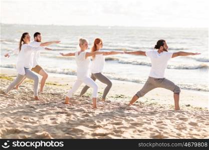 fitness, sport and healthy lifestyle concept - group of people making yoga in warrior pose on beach