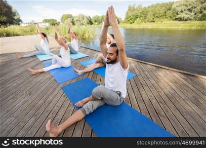 fitness, sport and healthy lifestyle concept - group of people making yoga exercise and meditating outdoors on river or lake berth