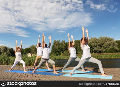 fitness, sport, and healthy lifestyle concept - group of people making yoga in warrior pose on river or lake berth