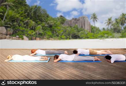 fitness, sport and healthy lifestyle concept - group of people making yoga exercises and lying on mats over tropical beach background. group of people making yoga exercises over beach