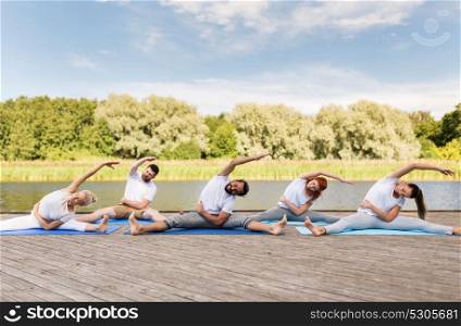 fitness, sport, and healthy lifestyle concept - group of people making yoga exercises outdoors on river or lake berth. group of people making yoga exercises outdoors