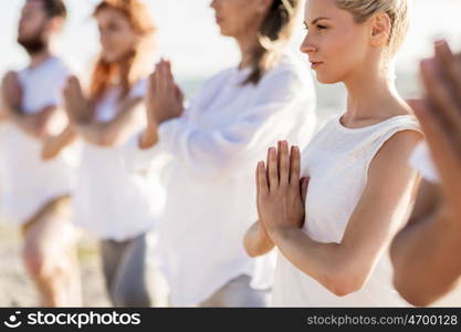 fitness, sport, and healthy lifestyle concept - group of people making yoga on beach