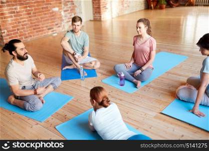 fitness, sport and healthy lifestyle concept - group of people with water bottles and towels in yoga class resting on mats at studio. group of people resting on yoga mats at studio