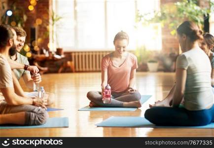 fitness, sport and healthy lifestyle concept - group of people with water bottles in yoga class resting on mats at studio. group of people resting on yoga mats at studio