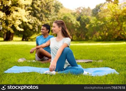 fitness, sport and healthy lifestyle concept - happy people doing yoga at summer park. happy people doing yoga at summer park