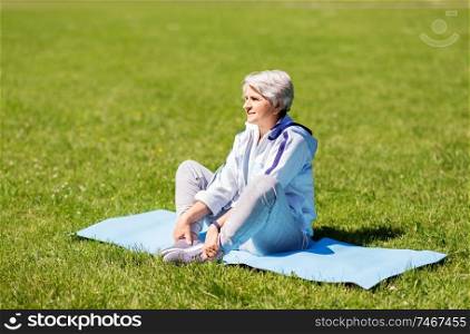 fitness, sport and healthy lifestyle concept - happy smiling senior woman exercising on mat at summer park. happy senior woman exercising at summer park