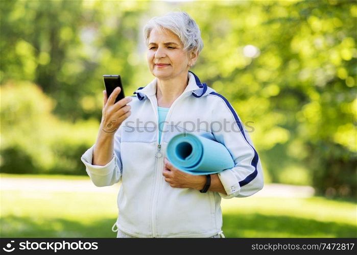 fitness, sport and healthy lifestyle concept - happy smiling senior woman with exercise mat and smartphone at park. old woman with exercise mat and smartphone at park
