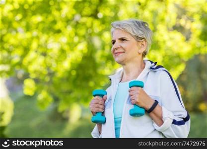 fitness, sport and healthy lifestyle concept - happy smiling senior woman with dumbbells exercising at summer park. senior woman with dumbbells exercising at park