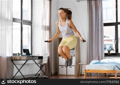 fitness, sport and healthy lifestyle concept - happy smiling teenage girl skipping with jump rope at home. teenage girl exercising with jump rope at home