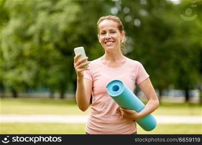 fitness, sport and healthy lifestyle concept - happy smiling woman with exercise mat and smartphone at summer park. woman with exercise mat and smartphone at park