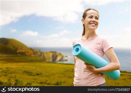 fitness, sport and healthy lifestyle concept - happy smiling woman with exercise mat over big sur coast of california background. happy smiling woman with exercise mat over big sur