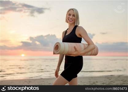 fitness, sport, and healthy lifestyle concept - happy smiling woman with yoga mat on beach over sunset. happy woman with yoga mat on beach