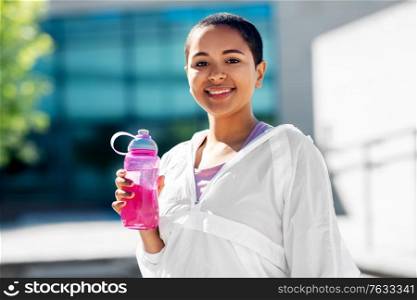 fitness, sport and healthy lifestyle concept - happy smiling young african american woman drinking water from bottle outdoors. african american woman drinking water from bottle
