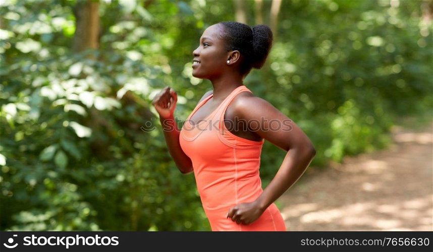 fitness, sport and healthy lifestyle concept - happy smiling young african american woman running in forest. young african american woman running in forest