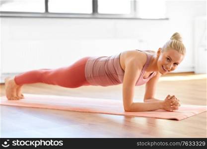 fitness, sport and healthy lifestyle concept - happy smiling young woman doing yoga in forearm plank pose at home. woman doing yoga in forearm plank pose at home