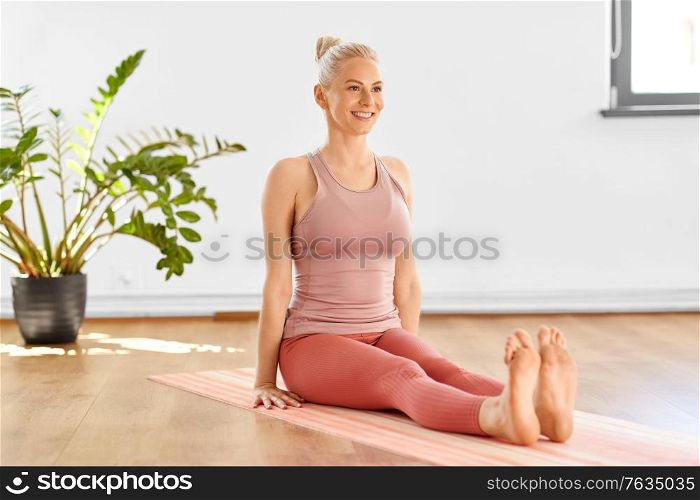 fitness, sport and healthy lifestyle concept - happy smiling young woman in seated pose on yoga mat at home. happy woman in seated pose on yoga mat at home