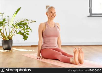 fitness, sport and healthy lifestyle concept - happy smiling young woman in seated pose on yoga mat at home. happy woman in seated pose on yoga mat at home