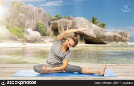 fitness, sport and healthy lifestyle concept - happy woman doing yoga and stretching on mat over exotic tropical beach background. happy woman doing yoga and stretching on beach