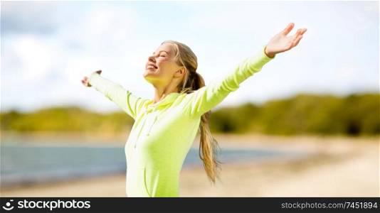 fitness, sport and healthy lifestyle concept - happy woman in sports clothes enjoying sun over summer beach background. happy woman in sports clothes on beach