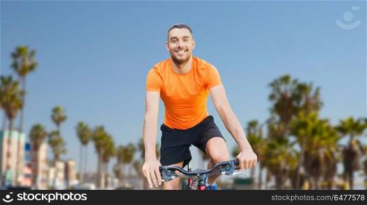 fitness, sport and healthy lifestyle concept - happy young man riding bicycle over venice beach background in california. happy young man riding bicycle over venice beach. happy young man riding bicycle over venice beach