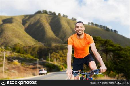 fitness, sport and healthy lifestyle concept - happy young man riding bicycle over big sur hills and road background in california. happy young man riding bicycle over big sur hills. happy young man riding bicycle over big sur hills