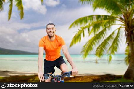 fitness, sport and healthy lifestyle concept - happy young man riding bicycle over tropical beach background in french polynesia. happy young man riding bicycle over tropical beach. happy young man riding bicycle over tropical beach
