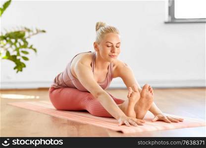 fitness, sport and healthy lifestyle concept - happy young woman doing yoga and seated forward bend at home. woman doing yoga and seated forward bend at home