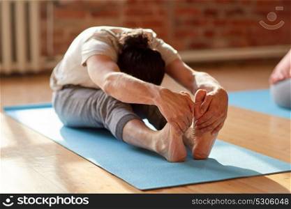 fitness, sport and healthy lifestyle concept - man doing yoga seated forward bend pose on mats at studio or gym. man doing yoga forward bend at studio or gym