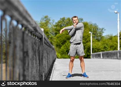 fitness, sport and healthy lifestyle concept - man stretching hand and shoulder on bridge. man stretching hand and shoulder on bridge