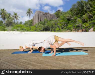fitness, sport and healthy lifestyle concept - people making yoga exercises outdoors over exotic tropical beach background. people making yoga exercises outdoors