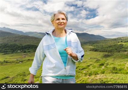 fitness, sport and healthy lifestyle concept - senior woman running over Killarney National Park valley in ireland background. senior woman running along summer park