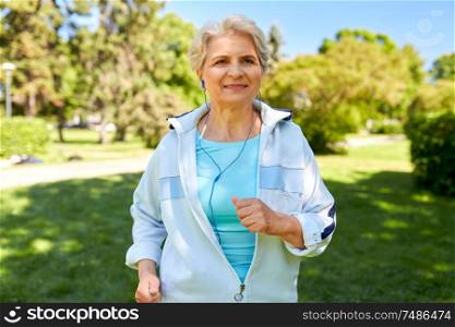 fitness, sport and healthy lifestyle concept - senior woman with earphones listening to music and running at summer park. senior woman with earphones running at summer park