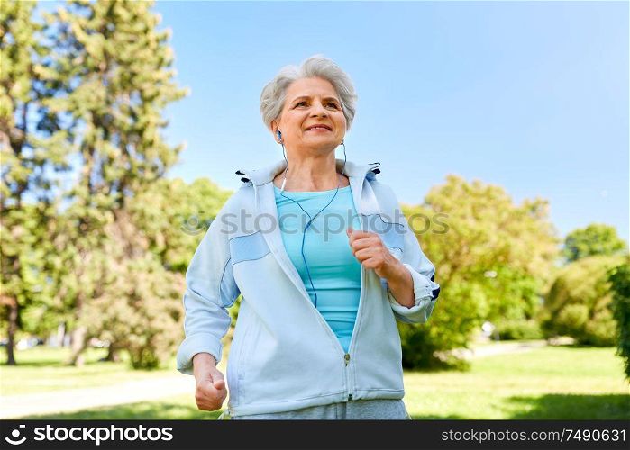 fitness, sport and healthy lifestyle concept - senior woman with earphones listening to music and running along summer park. senior woman with earphones running in summer park