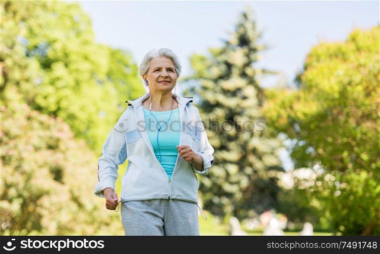 fitness, sport and healthy lifestyle concept - senior woman with earphones running along summer park. senior woman with earphones running in summer park