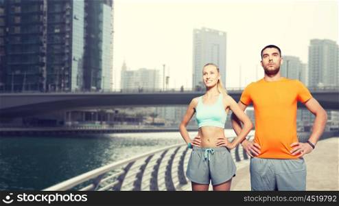 fitness, sport and healthy lifestyle concept - smiling couple exercising over dubai city street and waterside background