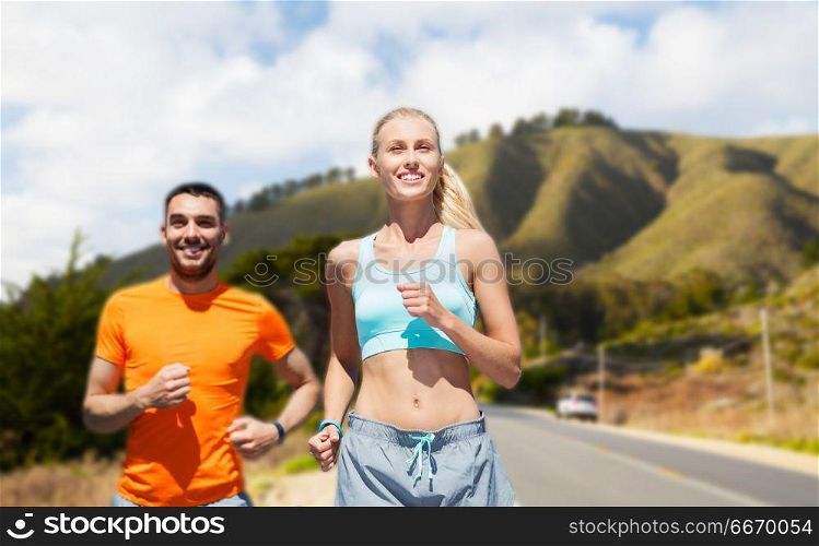 fitness, sport and healthy lifestyle concept - smiling couple running over big sur hills and road background in california. smiling couple running over big sur hills. smiling couple running over big sur hills