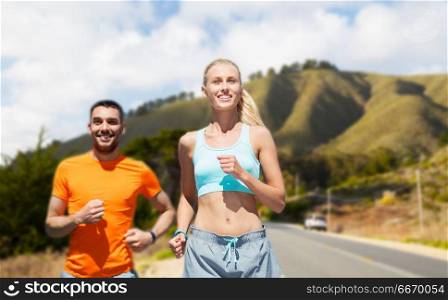 fitness, sport and healthy lifestyle concept - smiling couple running over big sur hills and road background in california. smiling couple running over big sur hills. smiling couple running over big sur hills