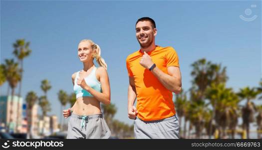 fitness, sport and healthy lifestyle concept - smiling couple with heart-rate watch running over venice beach background in california. couple running over venice beach background. couple running over venice beach background