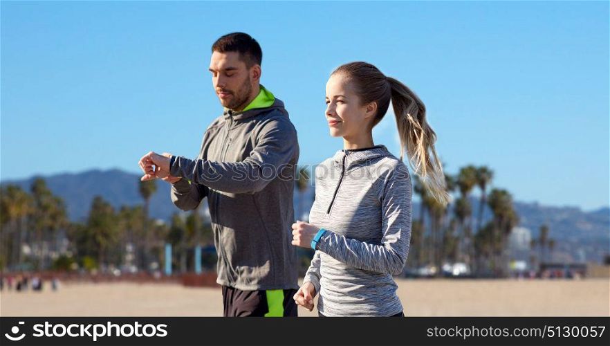 fitness, sport and healthy lifestyle concept - smiling couple with heart-rate watches running over venice beach background in california. couple with fitness trackers running outdoors. couple with fitness trackers running outdoors