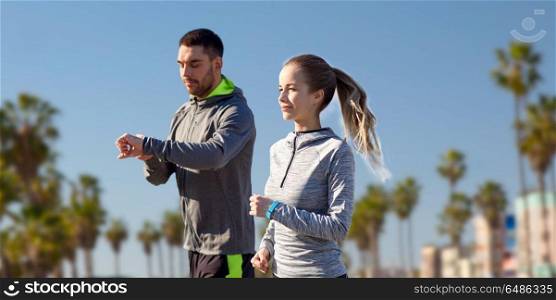 fitness, sport and healthy lifestyle concept - smiling couple with heart-rate watches running over venice beach background in california. couple with fitness trackers running outdoors. couple with fitness trackers running outdoors
