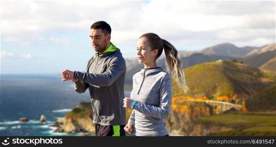 fitness, sport and healthy lifestyle concept - smiling couple with heart-rate watches running over bixby creek bridge on big sur coast of california background. couple with fitness trackers running outdoors. couple with fitness trackers running outdoors