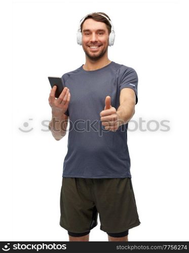 fitness, sport and healthy lifestyle concept - smiling man in sports clothes with smartphone and headphones listening to music and showing thumbs up over white background. man in sports clothes with phone and headphones