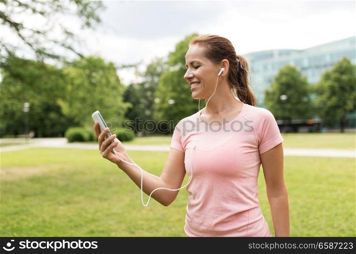 fitness, sport and healthy lifestyle concept - smiling woman listening to music on smartphone at park. woman listening to music on smartphone at park
