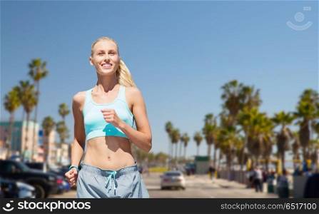 fitness, sport and healthy lifestyle concept - smiling woman running at summer over venice beach background in california. smiling woman running at summer over venice beach. smiling woman running at summer over venice beach