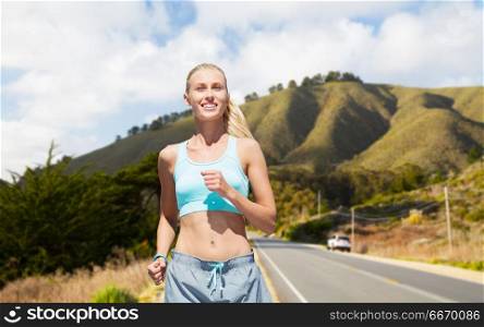 fitness, sport and healthy lifestyle concept - smiling woman running nearby road over big sur hills and road background in california. happy woman running nearby road over big sur hills. happy woman running nearby road over big sur hills